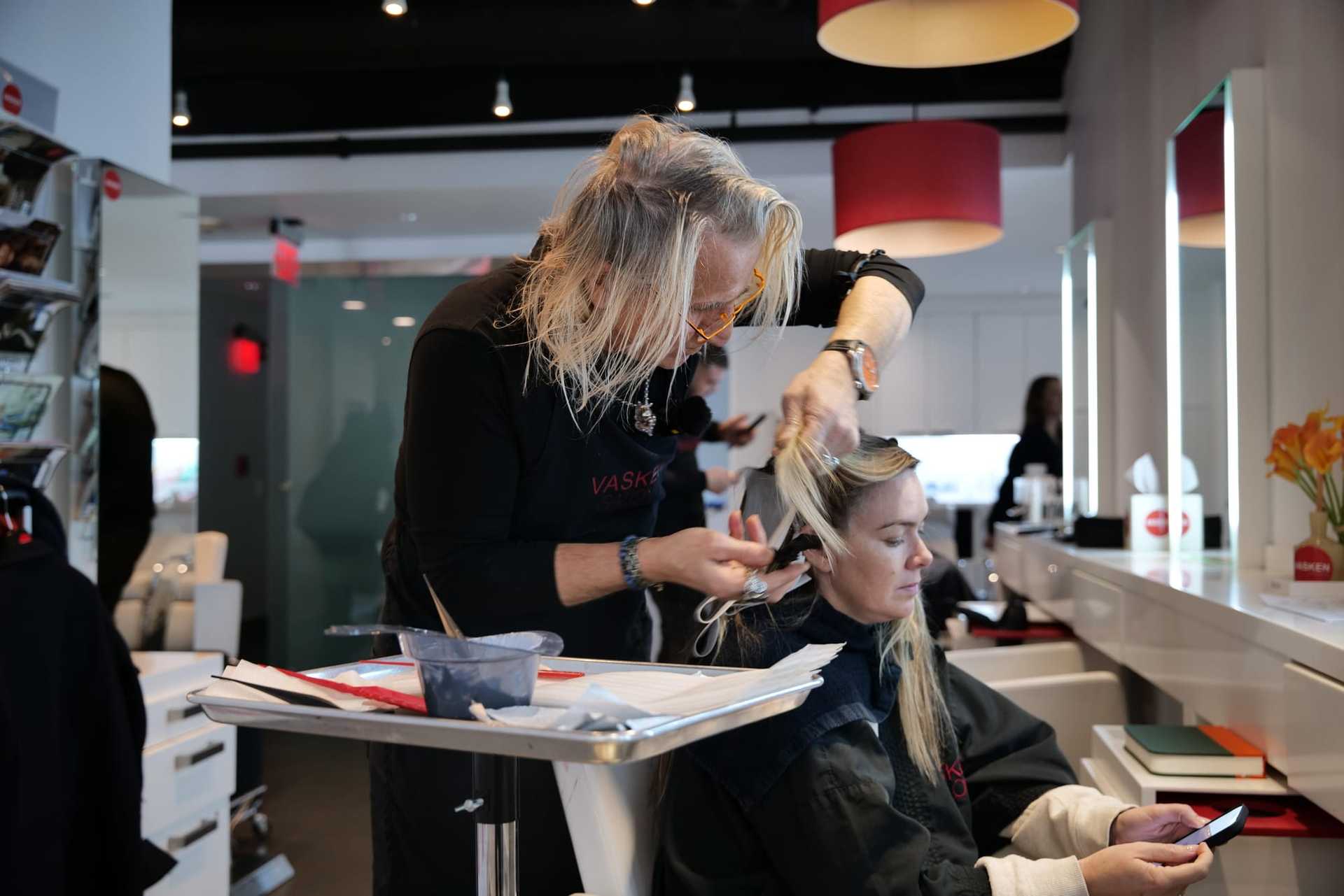 Hairdresser styles a woman's hair in a modern salon, with tools and products on a nearby counter.
